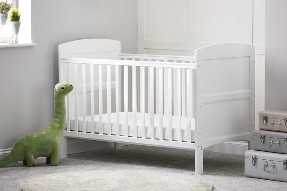 A green stuffed kangaroo near white cot bed in a kid's room.