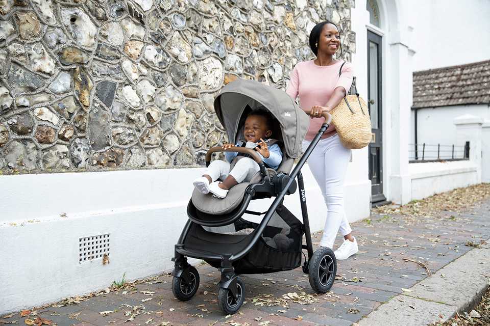 Shop pushchairs.A mother walking with her toddler in a Joie Versatrax pushchair in grey and black colour. 