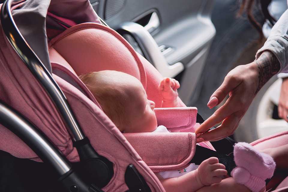 A mother putting her baby into a Red Kite Push Me Pace 2 in 1 travel system car seat in pink colour.