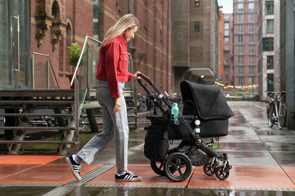 A mother walking with her baby in a Bugaboo Cameleon 3 plus complete pushchair in black colour.