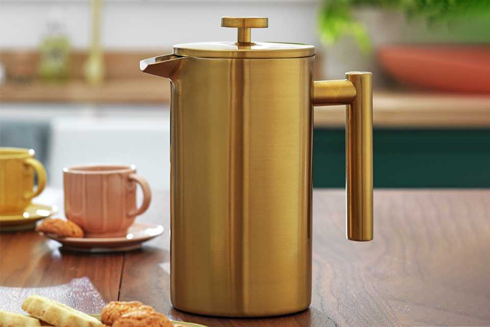 A Habitat double walled 8 cup cafetiere in gold finish placed on a wooden dining table.