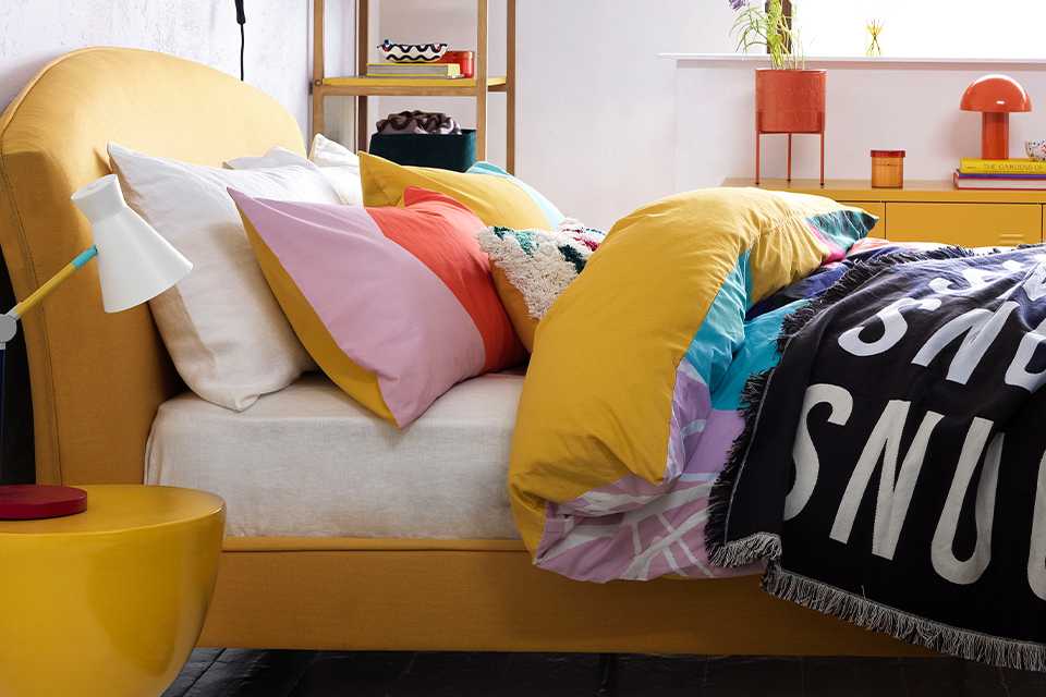 A bedroom with yellow bed and side table and multicoloured home accessories. 