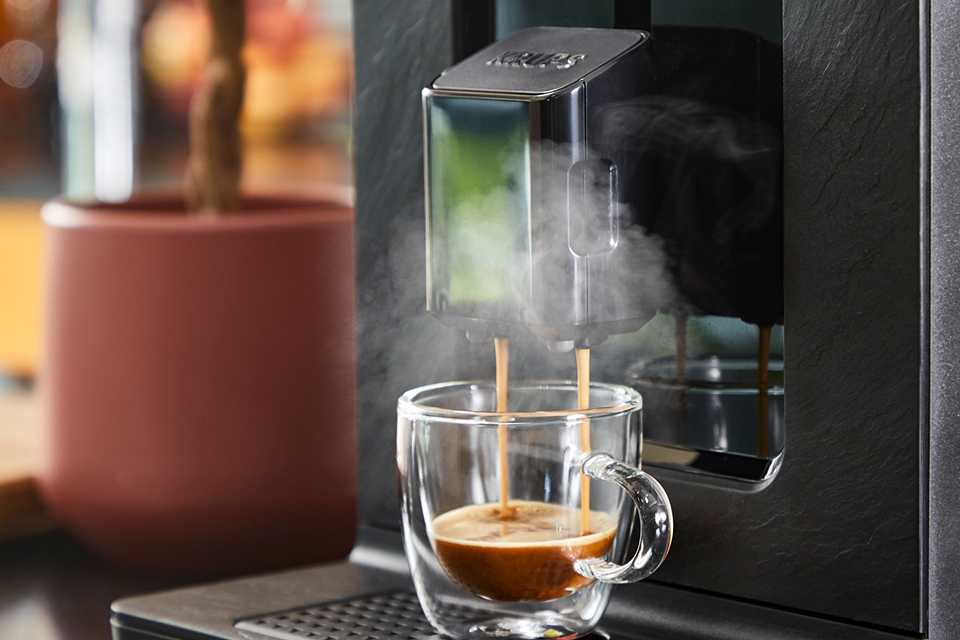 A Krups Bean to Cup Coffee Machine pours a hot shot of espresso into a glass mug.