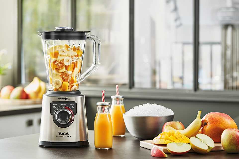 A Tefal Perfect Mix 2L Glass Jug Blender filled with fruit on a counter with 2 smoothies beside it