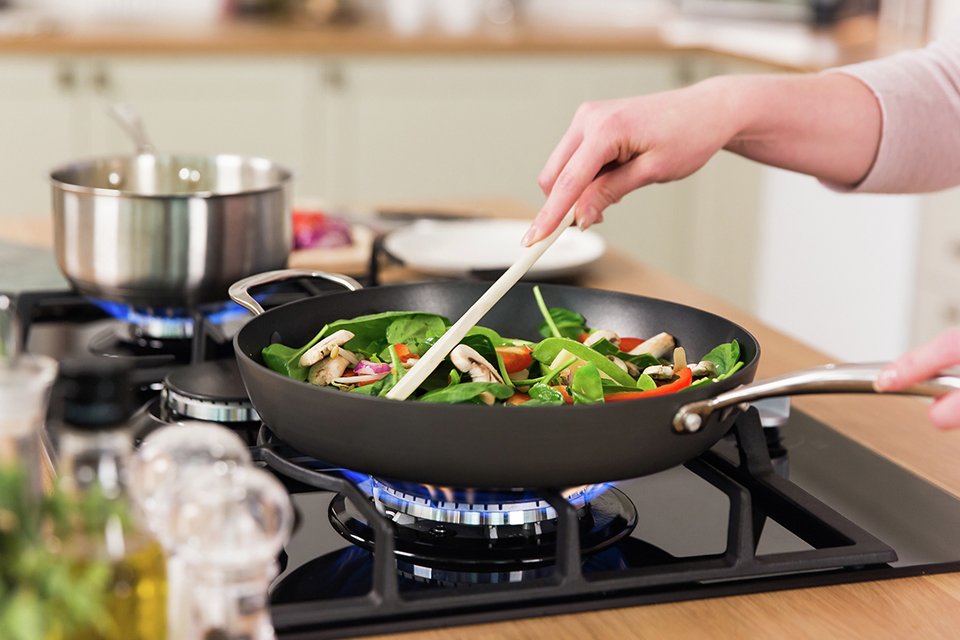 A woman cooking veggies on a Russell Hobbs black gas hob.