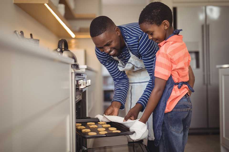 Father taking tray of fresh cookies out of oven with his son.