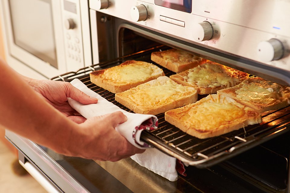 A person putting a tray of cheese on toast in the oven.