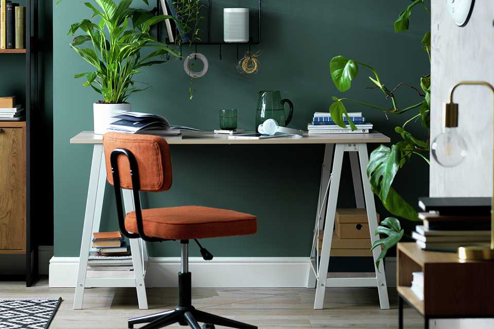 Green office space with wooden table and orange office chair and home accessories.