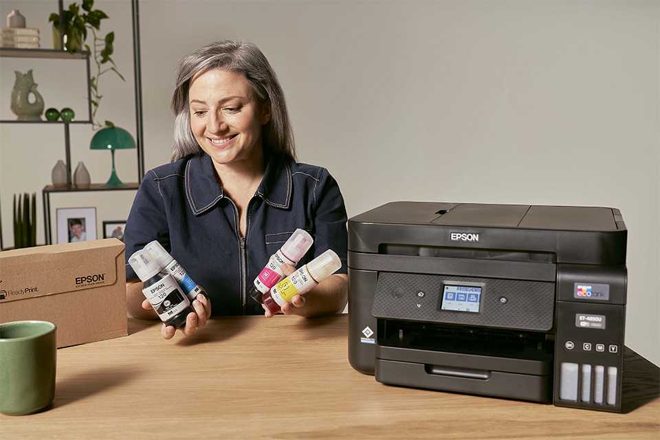 A lady holding 4 EcoTank ink bottles next to an Epson printer.