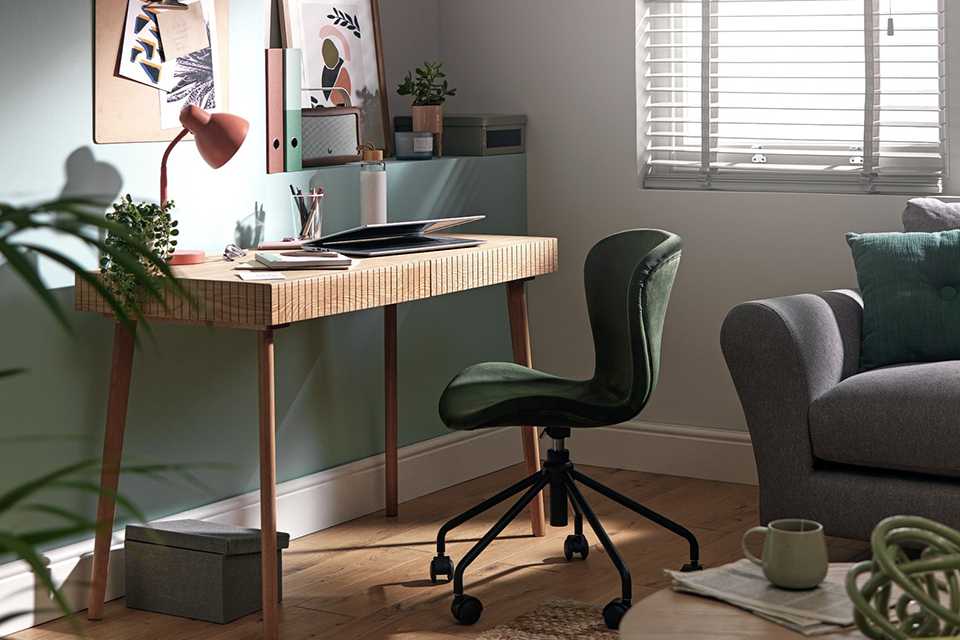 Wooden desk with green velvet office chair in home office.