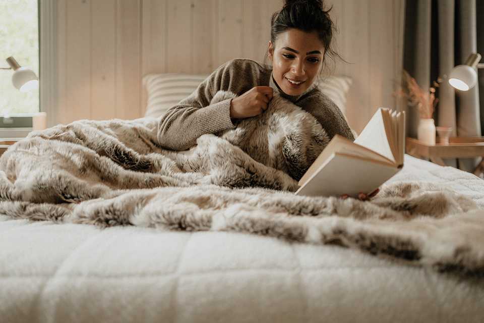 A woman reading a book covered in a Dreamland Scandi style dual control underblanket.