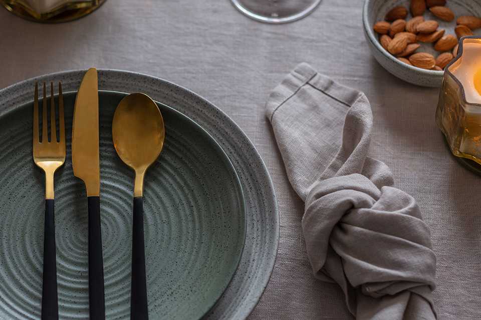 A place setting of grey dinnerware and gold and black cutlery.