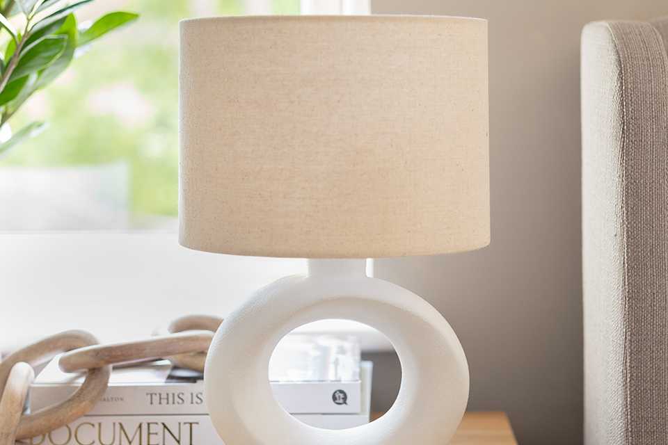 A white table lamp on a wooden finish bedside table. 