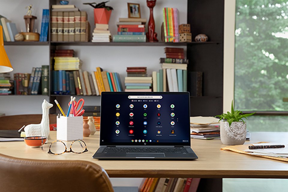 A laptop placed on a desk with a pair of spectacles, a pen holder, an indoor plant and other items.