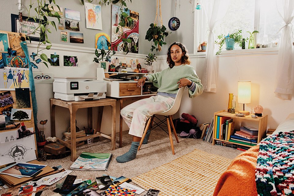 A lady sitting in a messy studyroom with an HP printer on the desk.