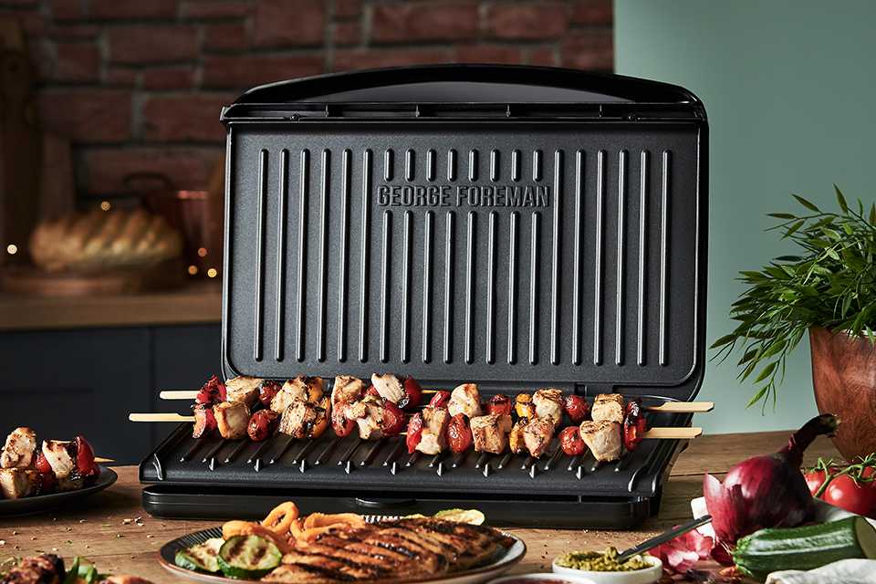 A George Foreman large grill on a wooden table with grilled food items.