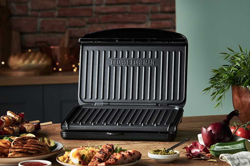 A George Foreman medium grill on a wooden table with grilled food items.