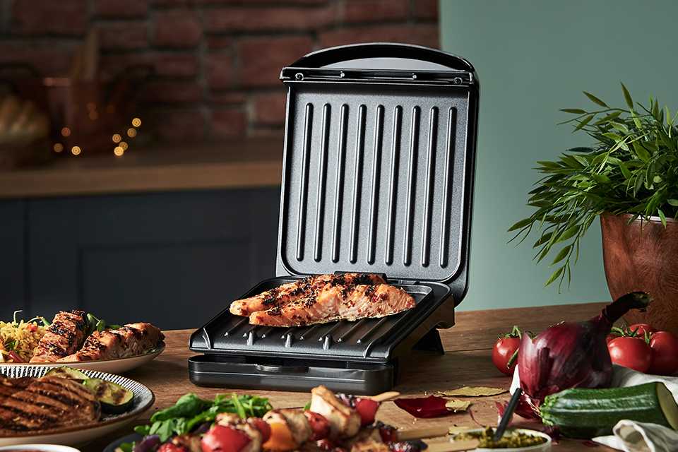 A George Foreman small grill on a wooden table with grilled food items.