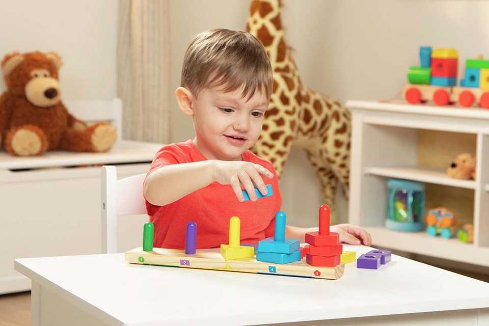 A boy playing with a Melissa and Doug stack sort board toy.