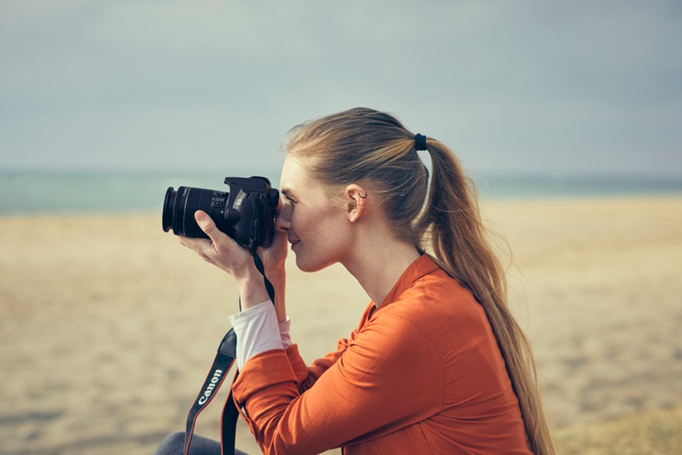 A woman taking photographs with a Canon DSLR camera at the beach. 