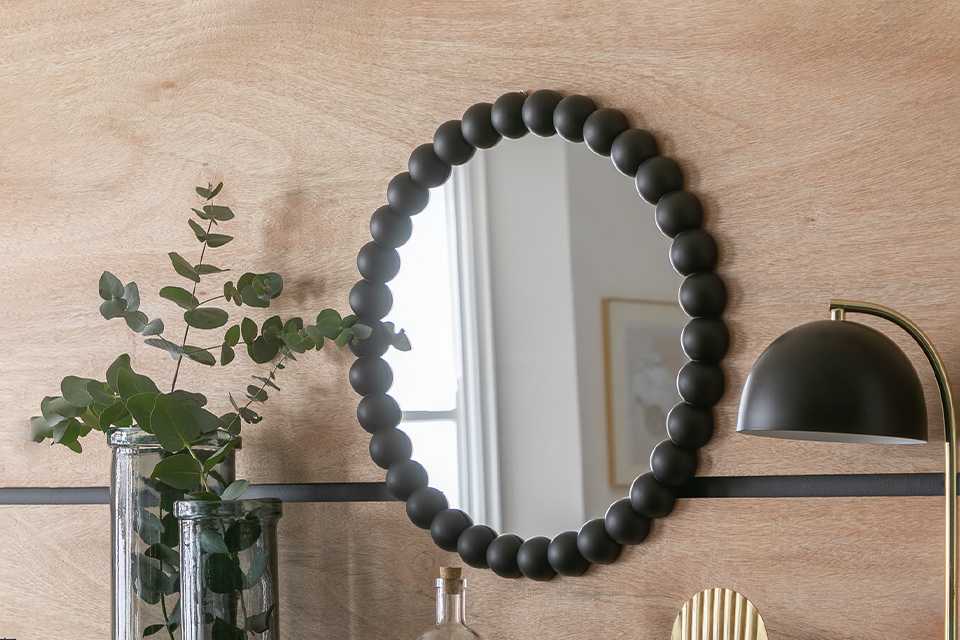Black beaded round wall mirror on a wooden wall.