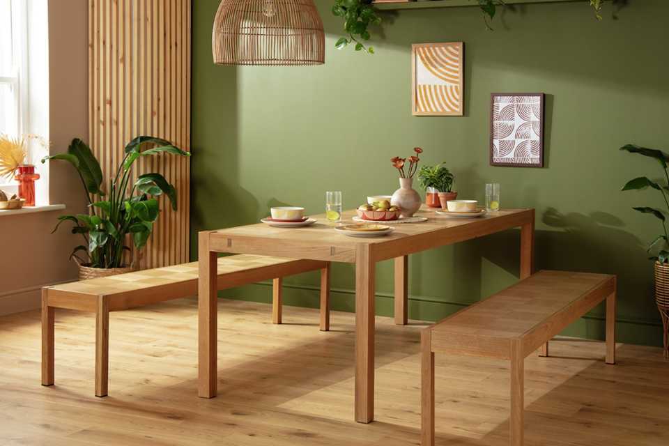 A wooden dining table and bench set placed in a green coloured dining room. 