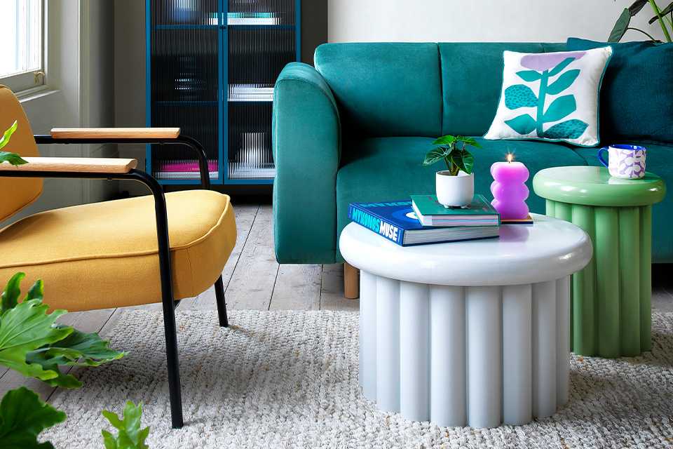 A living room with teal coloured sofa, a green side table, a white coffee table, and a yellow armchair.