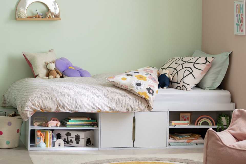 A kid's room with white cabin bed with storage and floral print reversible bedding.