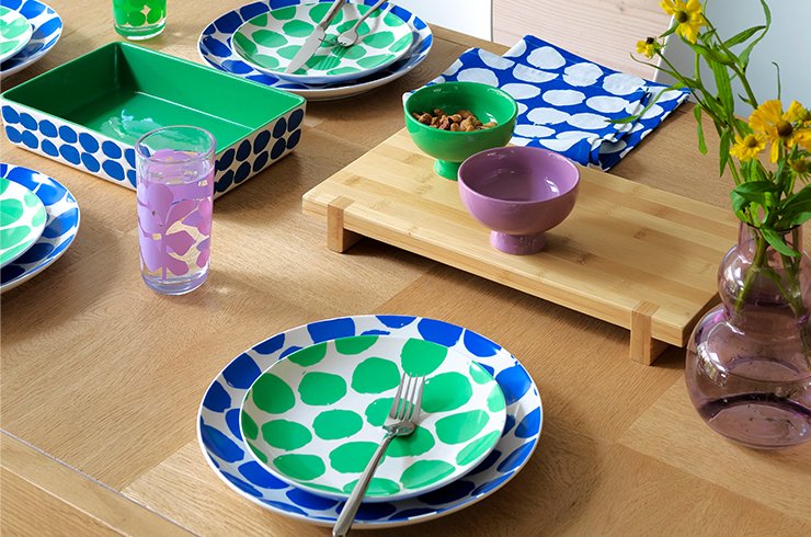 Green, yellow and pattterend cookware and tableware on a walnut effect dining table.