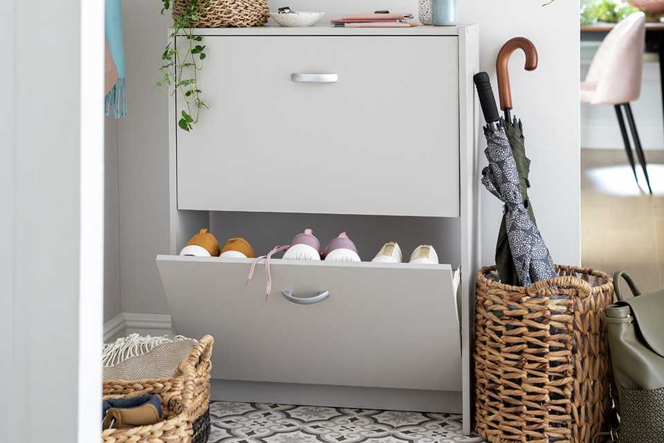 A white shoe storage cabinet in a hallway next to a basket with umbrellas in it.