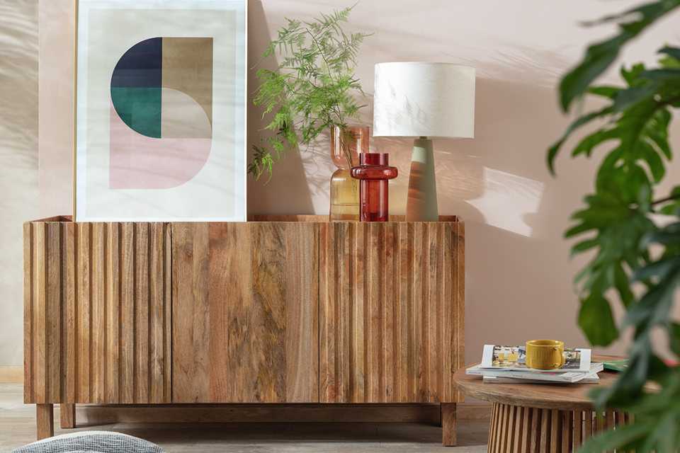 A wooden sideboard with a wall art, a pair of vases, and table lamp on it.