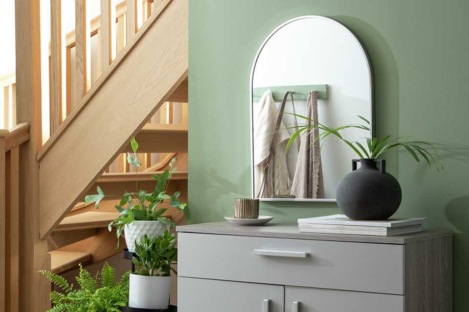 An arch wall mirror over a cabinet in a hallway.