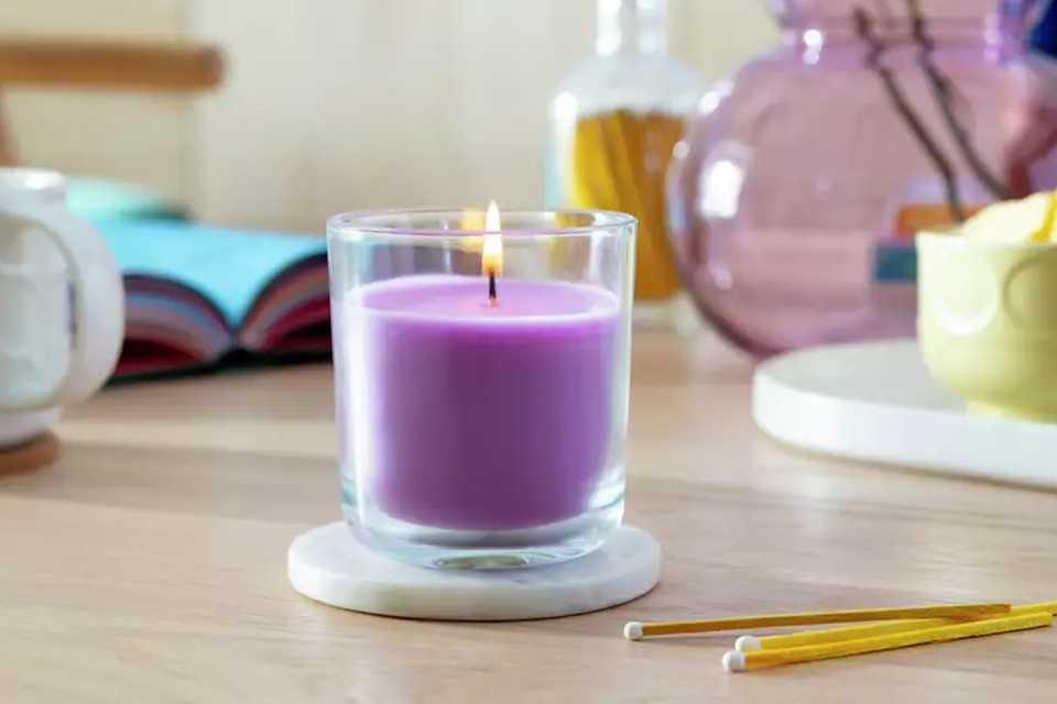 A lilac candle in a transparent candle holder on a table.