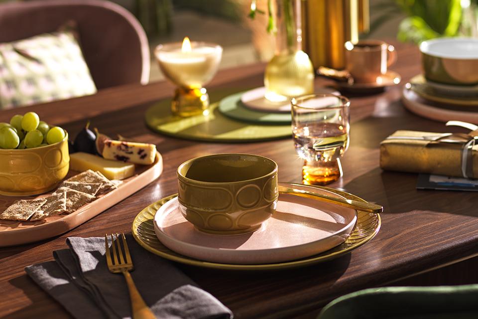 A wooden dining table with glazed stoneware nibble bowls, dinner set and glassware in green, yellow and white.