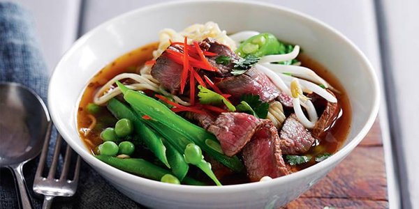 Bowl of Thai beef noodle soup with cutlery.