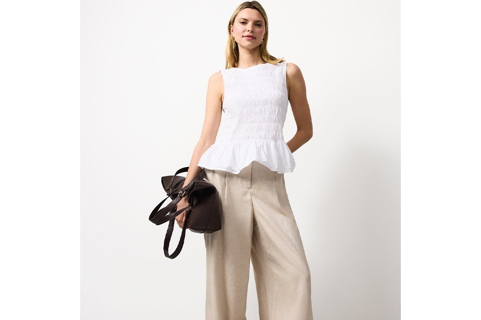 A women wearing a white two and neutral linen trousers carrying a handbag. 
