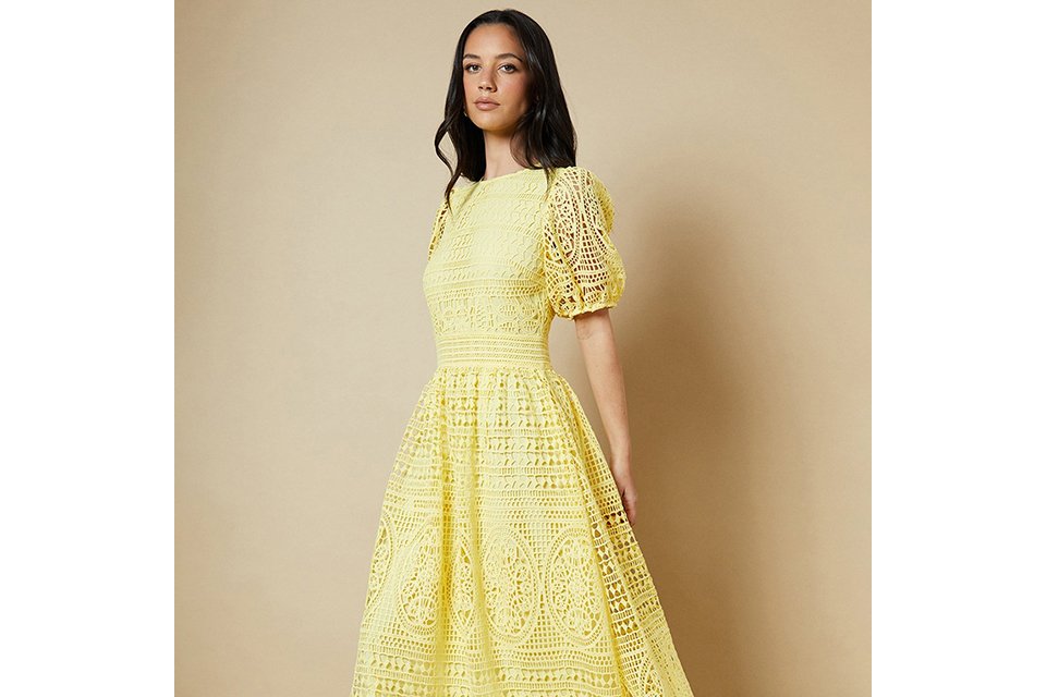 Black floral printed occasion dress with layered ruffle detailing, long sleeves and a high neckline, styled against a clean studio background.