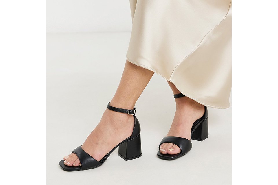 Black block‑heel ankle strap sandals styled with a cream satin midi skirt on a clean studio background.