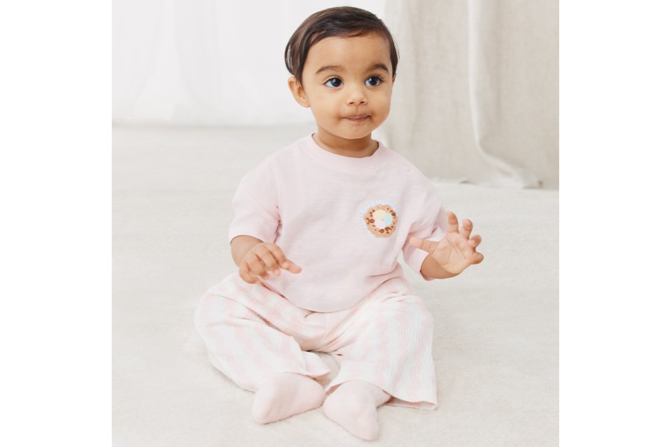 Baby girl wearing a pink top and pink and white gingham bottoms.