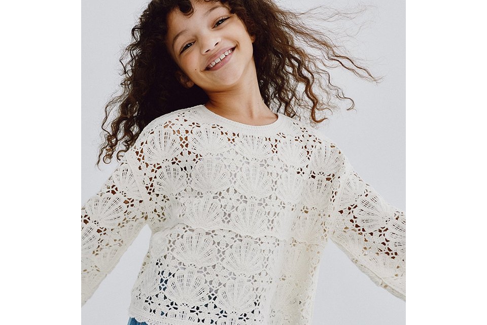 A young girl wearing a white crochet top and blue jeans.