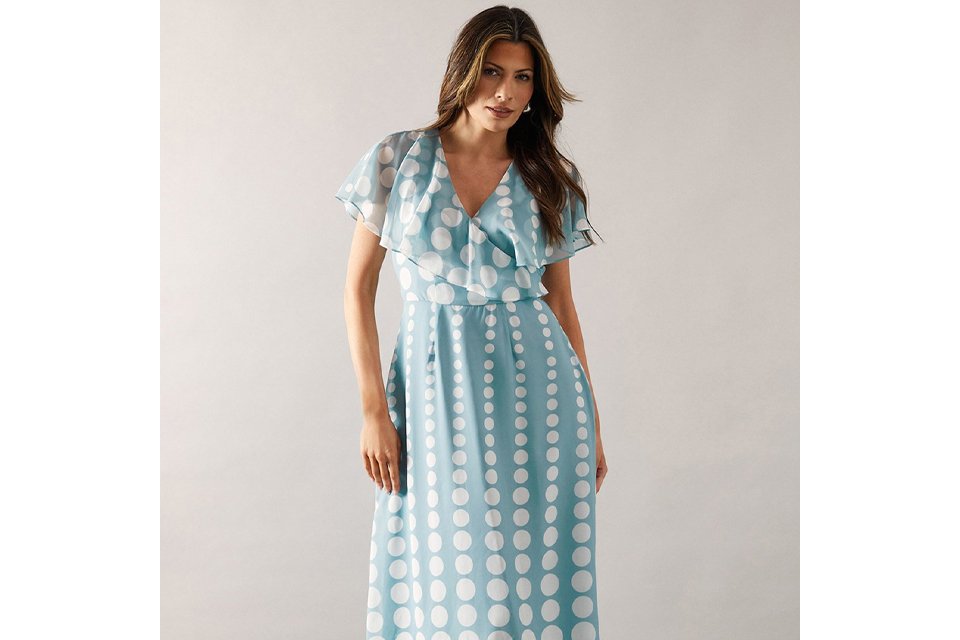 Woman wearing a pale blue dress with white polka dots and white stripey heels.
