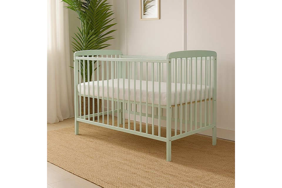 Pale green baby cot with mattress and plant in the background.