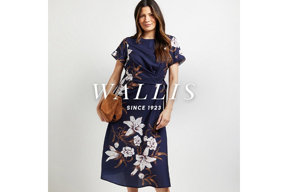 Person wearing a navy midi dress with large floral prints and a side-tied waist, holding a tan clutch.