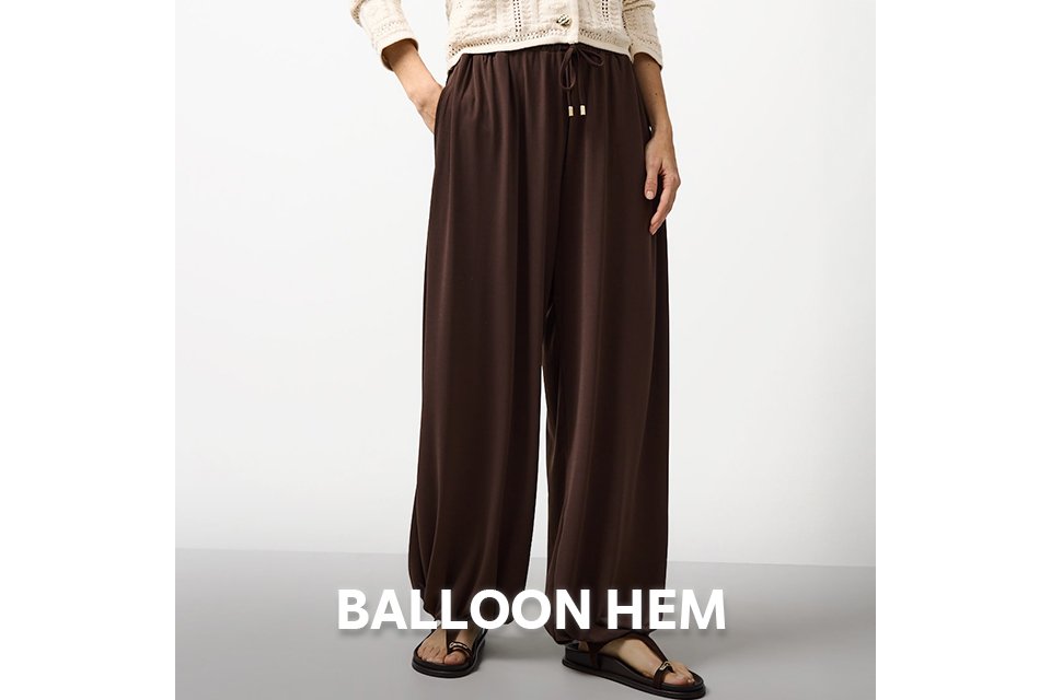 Woman wearing brown balloon trousers and cream neutral cardigan.