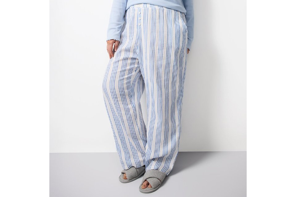 Women’s pastel green and white striped button‑up pyjama set with scalloped detailing, shown in a relaxed seated pose.