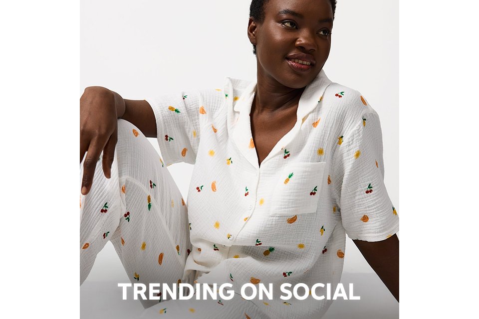 Person wearing a pink and red satin pajama set with a diamond pattern and decorative motifs, paired with beige slippers, standing against a plain white background.