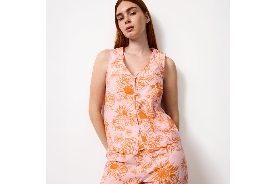 Women’s yellow floral satin pyjama top with purple and green botanical print, shown in a relaxed seated pose.