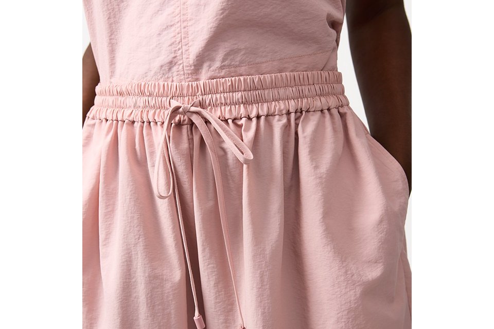 Cream sleeveless top and matching skirt styled with a black cut‑out bucket bag and crossbody strap on a neutral studio background.