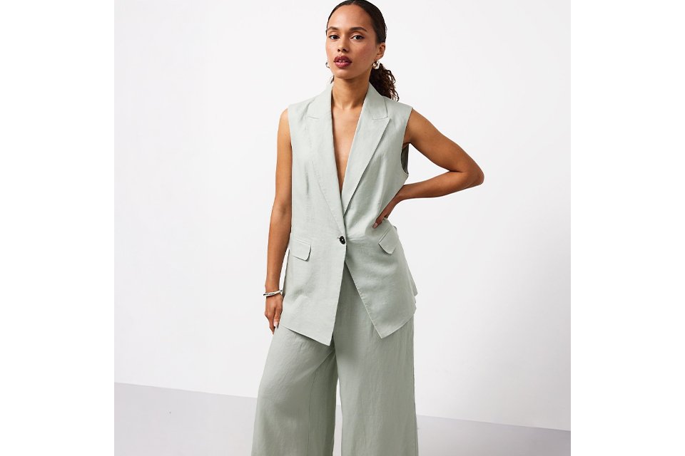 Black tailored blazer and belt styled with a green and blue patterned midi skirt, black heeled sandals and a black shoulder bag on a white background.