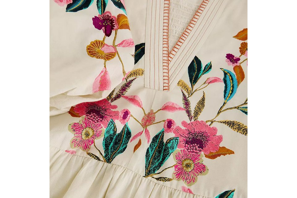 Pink floral tiered midi dress with short flutter sleeves and V‑neckline, styled with neutral heeled sandals on a light studio background.